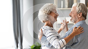 Happy romantic older retired family couple dancing at home.