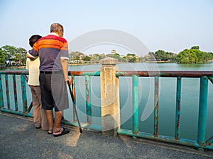 Happy romantic senior asian couple stand on the bridge in front of the lake. Husband stands with his wife. Concept of senior coupl