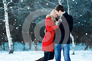 Happy romantic young couple walking in winter park on flying snowflakes snowy