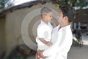 Happy rural indian young father and little son looking at each other and laughing wearing white traditional cloths with village