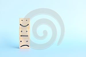 Happy, sad and angry face symbol on wooden blocks in blue background with copy space. Customer service rating, evaluation