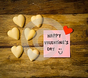 Happy Saint valentines day with post it note and heart shaped chocolate frame on wooden table