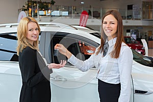 Happy saleswoman handing over car keys to the attractive young female owner