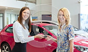 Happy saleswoman handing over car keys to the attractive young female owner of the new car