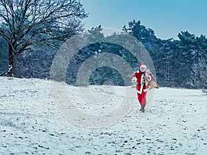 Happy Santa Claus with a big bag of gifts walks merrily to the side in a snowy winter forest. Christmas holiday concept