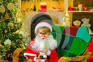 Santa Claus child eating a cookie and drinking glass of milk at home. Santa child boy picking cookie. Greeting card for