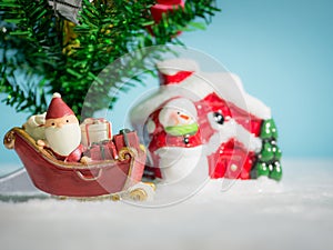 Happy Santa Claus with gifts box on the snow sled going to house. near house have Snowman and Christmas Tree. Santa Claus