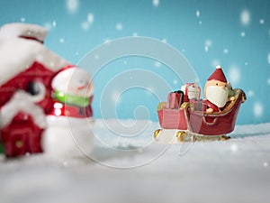 Happy Santa Claus with gifts box on the snow sled going to snow house. near snow house have Snowman and Christmas Tree.