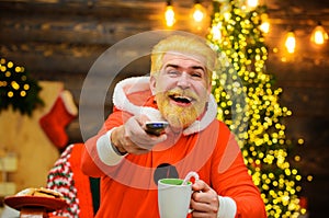 Happy Santa Claus with hot drink watching Christmas movie. Entertainment and cinema. New year background.
