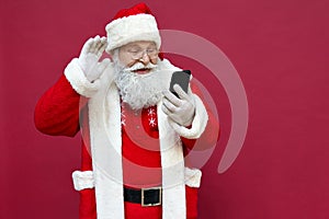 Happy Santa Claus video calling using smart phone isolated on red background.