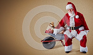 A happy Santa Claus with a wheelbarrow full of Christmas presents on a plain background with copy space