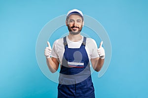 Happy satisfied handyman in overalls and hygiene gloves showing thumbs up, profession of service industry