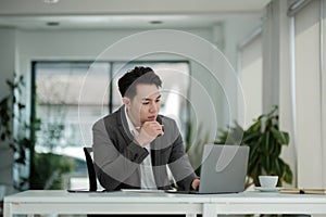 Happy satisfied millennial man using laptop at office workplace, working from home, reading message with good news