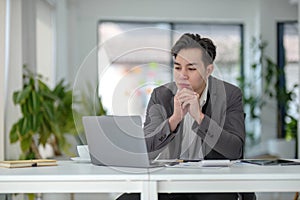 Happy satisfied millennial man using laptop at office workplace, working from home, reading message with good news