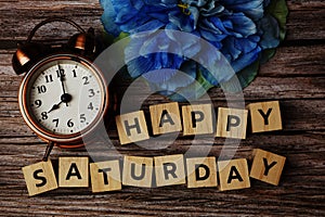 Happy Saturday alphabet letter with alarm clock on wooden background