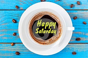 Happy saturday written on Coffee Cup at blue wooden background with beans