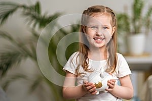 Happy savings. A little cute girl with a piggy Bank on the home background