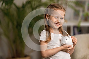 Happy savings. A little cute girl with a piggy Bank on the home background