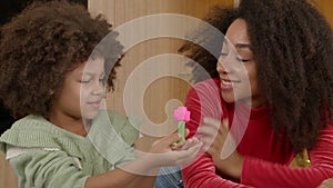 Happy school age black daughter surprising mother with handmade playdough toy