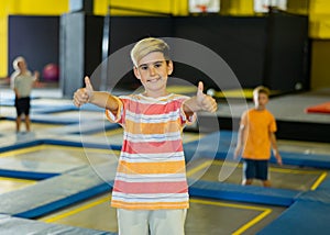 Happy school-age boy showing ok gesture during free time on trampolines in entertainment center
