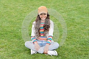 Happy school age female child smile sitting on green grass, girl