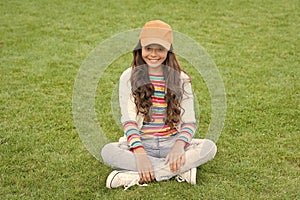 Happy school age female child smile sitting on green grass, girl