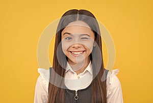 Happy school age girl child with smiling face give wink yellow background, winking
