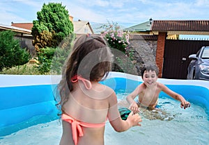 Happy school age kids play ball and splashing each other with water in inflatable swimming pool during summer holidays