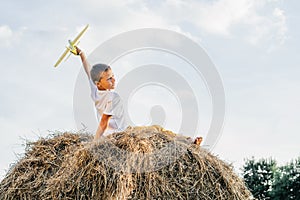 Happy school aged boy sitting at top of haystack launch toy airplane. Carefree child on haymaking play toys.