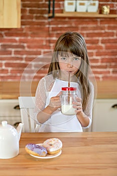 Happy school girl eating donuts and drinking milk on the kitchen at home. Tasty food for kids. Homemade food concept
