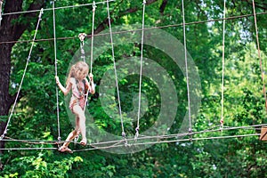 Happy school girl enjoying activity in a climbing adventure park on a summer day,