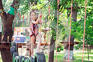 Happy school girl enjoying activity in a climbing adventure park on a summer day,