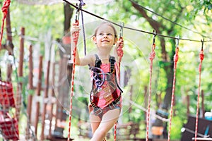 Happy school girl enjoying activity in a climbing adventure park on a summer day,