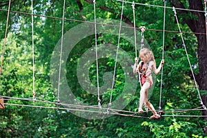 Happy school girl enjoying activity in a climbing adventure park on a summer day,