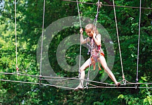 Happy school girl enjoying activity in a climbing adventure park on a summer day,