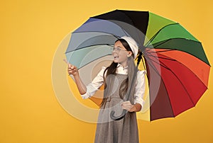 happy school girl in glasses. teen child under colorful parasol pointing finegr.