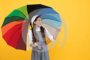 happy school girl in glasses. teen child under colorful parasol pointing finegr.