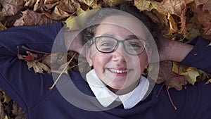 Happy school girl lies on autumn leaves and smiling
