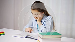 Happy school girl reading book or textbook at home