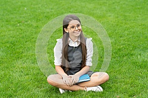 Happy school girl teenager sitting legs crossed on grass. School and education. Back to school