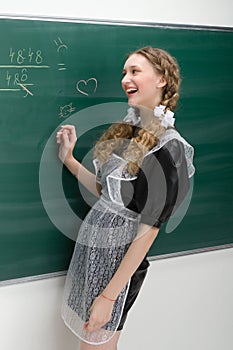 Happy school girl in uniform writing at blackboard