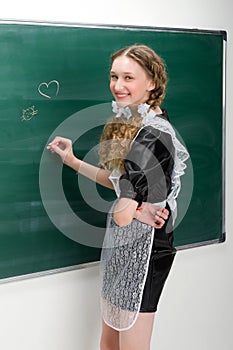 Happy school girl in uniform writing at blackboard