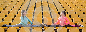 Happy school girls teenagers in activewear do splits stretching legs on stadium seats, endurance