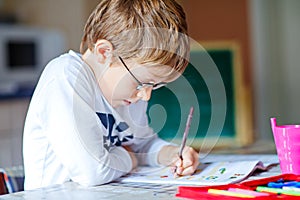 Happy school kid boy with glasses at home making homework