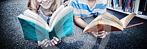 Happy school kids lying on floor and reading a book in library