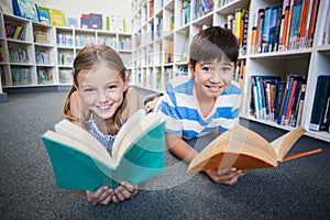 Happy school kids lying on floor and reading a book in library