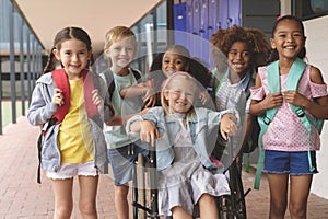 Happy school kids standing in corridor while schoolgirl sitting on wheelchair