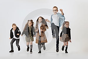 Happy school and preschool age children, girls and boys running, jumping isolated on grey studio background. Beauty