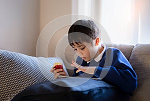Happy schoolboy eating red apple while playing game online with friend on tablet,Kid using internet sending homework to the