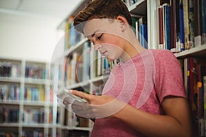 Happy schoolboy using digital tablet in library